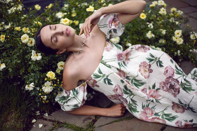 Outdoor portrait of a beautiful girl in a dress lying on the ground next to a white roses