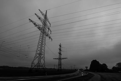 Low angle view of silhouette electricity pylons against sky