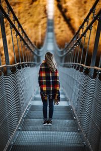 Rear view of young woman standing on footbridge in forest during autumn