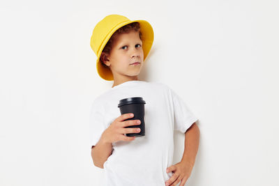 Portrait of boy holding coffee cup standing against white background