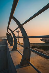 Metal railing by sea against clear sky during sunset