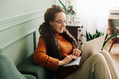 Young woman using laptop while sitting on sofa at home