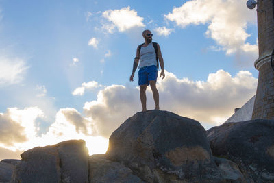 Rear view of man standing on rock against sky