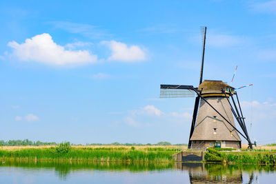 Traditional windmill by lake against sky