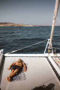 Full length of shirtless man lying on catamaran against sky during sunny day