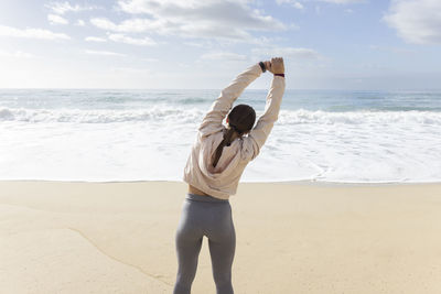 Sportswoman stretching arms at beach on sunny day