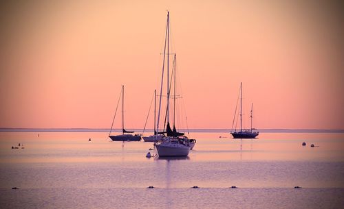 Boats sailing in sea against clear sky during sunset