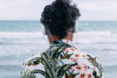 Back man listens to music while looking at the sea on the beach
