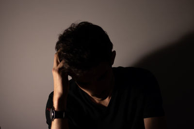 Sad young man against wall in darkroom