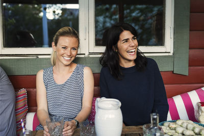 Portrait of happy woman sitting on friend in log cabin