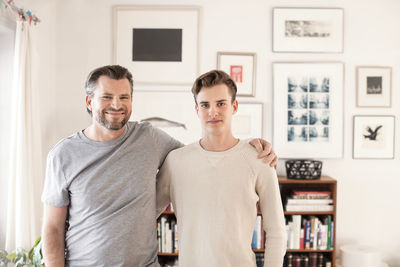 Portrait of confident father and son standing with arms around at new home