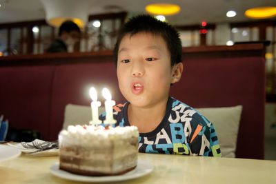 Boy looking at lit candles on cake at restaurant