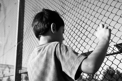 Rear view of boy standing by chainlink fence