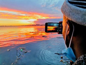 Rear view of man photographing sea against sky during sunset