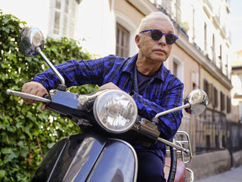 Low angle of smiling woman in vintage outfit sitting on retro motorbike and cheerfully looking away