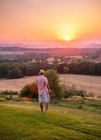 Rear view of man on field against sky during sunset