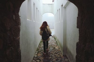 Rear view of woman standing in alley amidst buildings