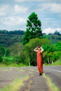 Young woman wearing sunglasses standing on road against trees in forest