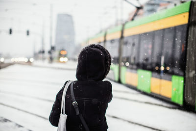 Rear view of woman standing by tramway in city during winter