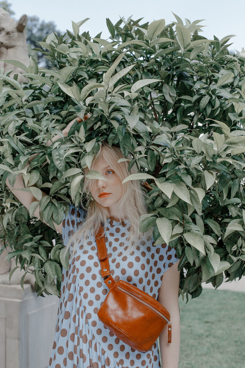 plant, one person, real people, blond hair, leisure activity, lifestyles, standing, front view, women, portrait, green color, hair, young women, young adult, casual clothing, three quarter length, growth, looking at camera, hairstyle, beautiful woman, outdoors, teenager