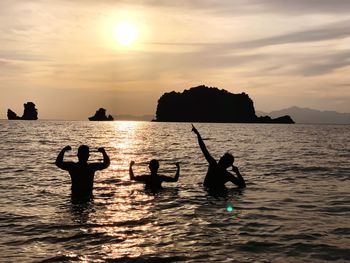 Silhouette people enjoying in sea against sky during sunset