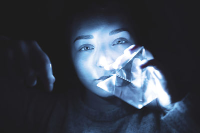 Close-up portrait of young woman holding quartz in darkroom