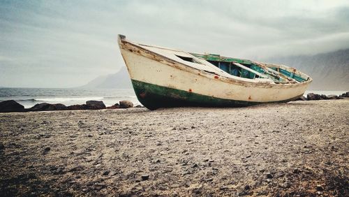 Abandoned boat moored on beach against sky