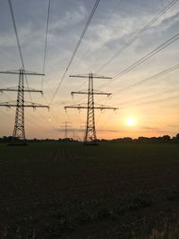 Silhouette electricity pylon on field against sky at sunset