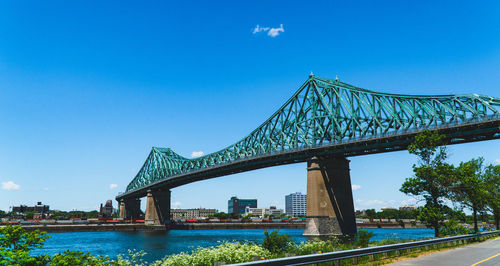 Low angle view of bridge over river against blue sky