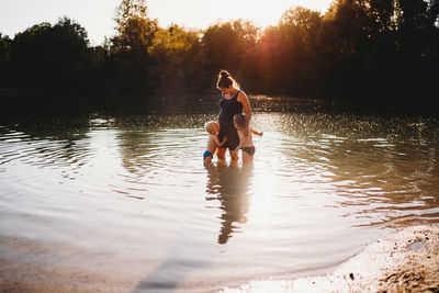 Kids kissing pregnant mother's belly in water at lake during sunset