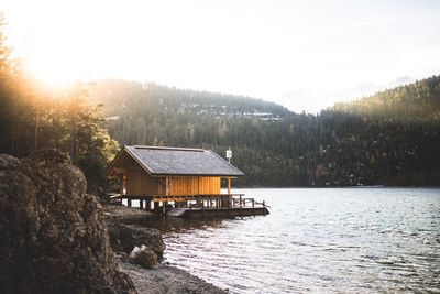 Stilt house on lake against sky during sunset