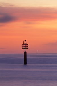 Lighthouse by sea against romantic sky at sunset