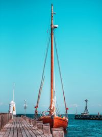 Sailboat moored at harbor on sea against clear blue sky