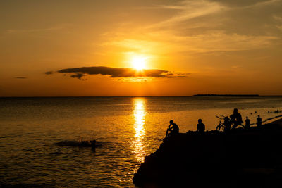 Silhouette people on sea against sky during sunset