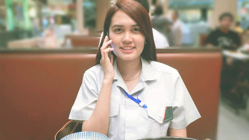 Portrait of smiling woman talking on mobile phone while sitting at restaurant