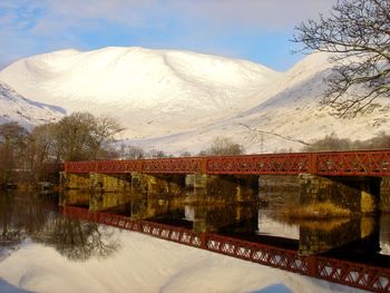 Bridge over lake by snowcapped mountains against sky