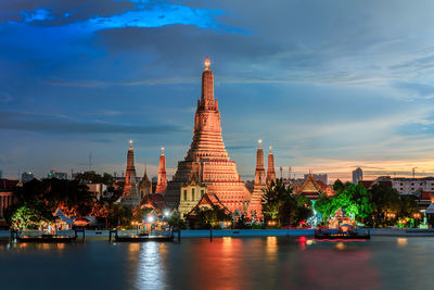 Illuminated buildings by river against sky in city