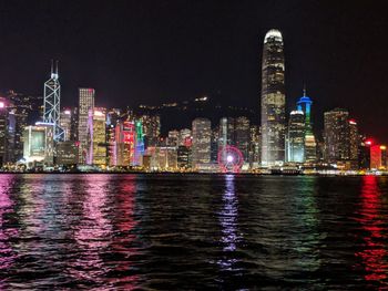 Illuminated buildings by river against sky in city at night