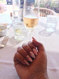 Cropped hand of woman showing nail art by drink on table