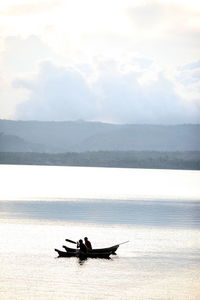 People sailing on rowboats in river against sky