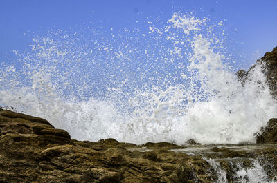 Waves splashing on rocks against sky