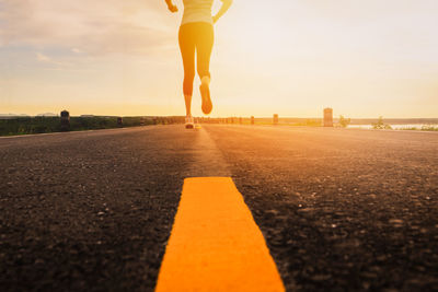 Low section of woman on road against sky during sunset