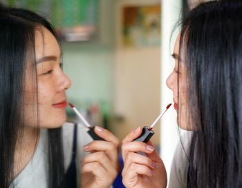 Close-up of young woman applying make-up reflecting on mirror