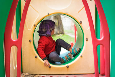 Rear view of boy sitting on slide at playground
