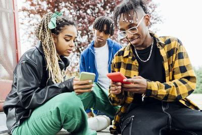 Young man and woman using smart phone sitting in front of friend