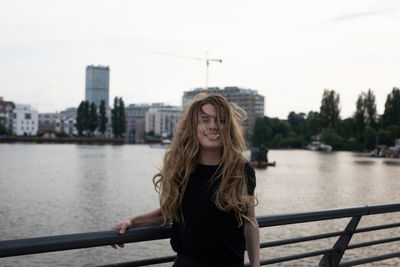 Portrait of beautiful woman standing by railing against river