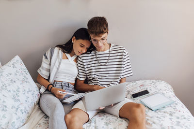 Girl studying with brother on laptop in bedroom at home