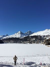 Rear view of woman standing by frozen lake at swiss alps against clear blue sky