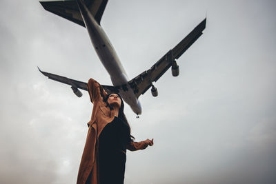 Low angle view of man looking at airplane against sky