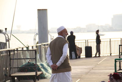 Rear view of mature man with hands behind back standing at promenade